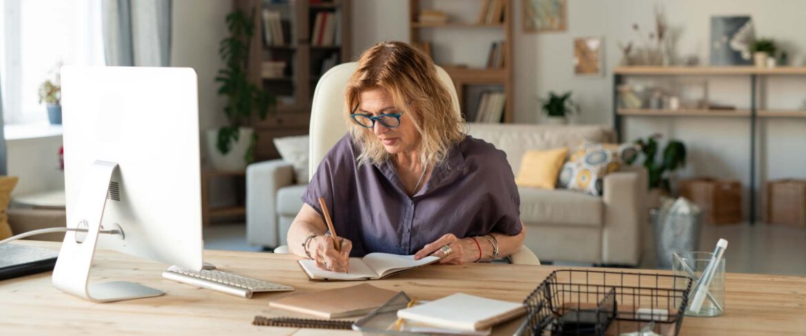 woman working at desk, writing on notebook while in her home office