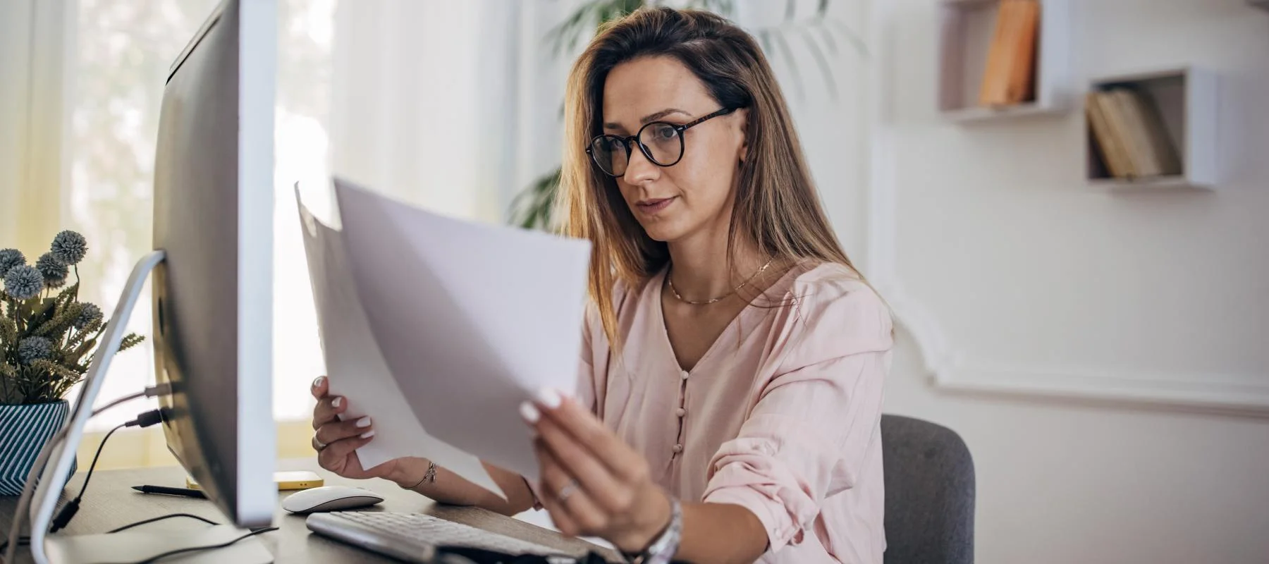 Woman with glasses looking at sheets of paper in a professional setting.