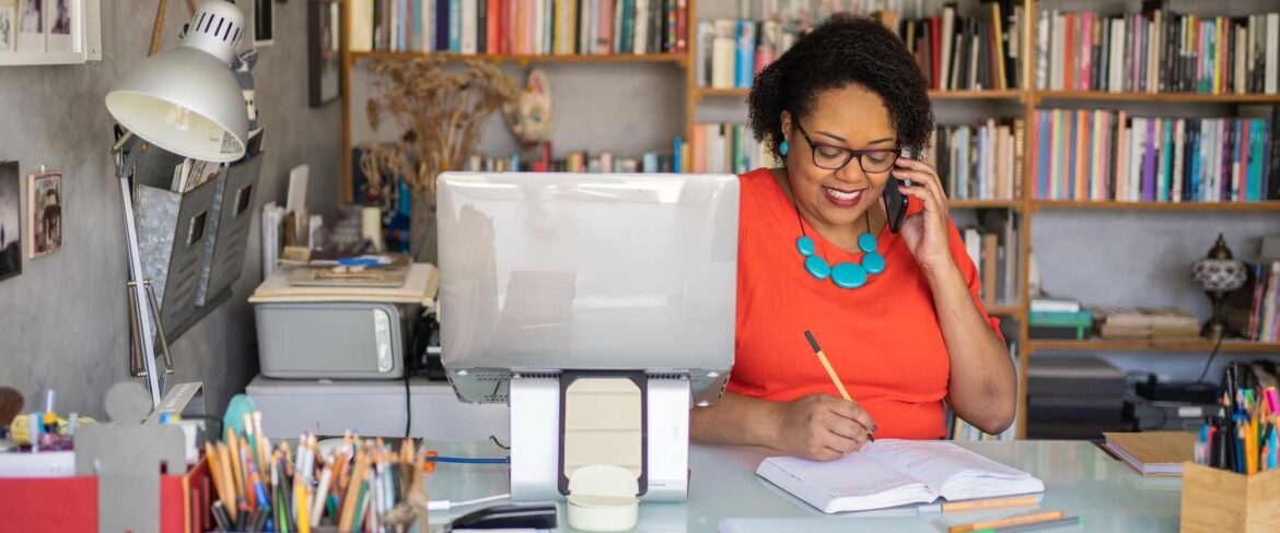 Executive assistant sitting at desk, working on computer with bright dress and green necklace on.