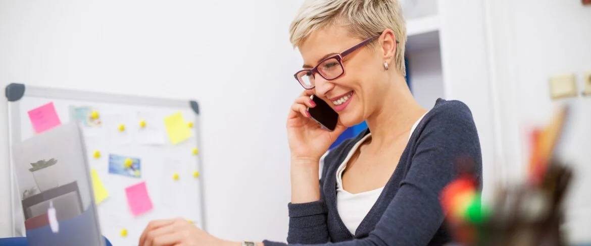 Woman with glasses on phone, looking at computer screen.