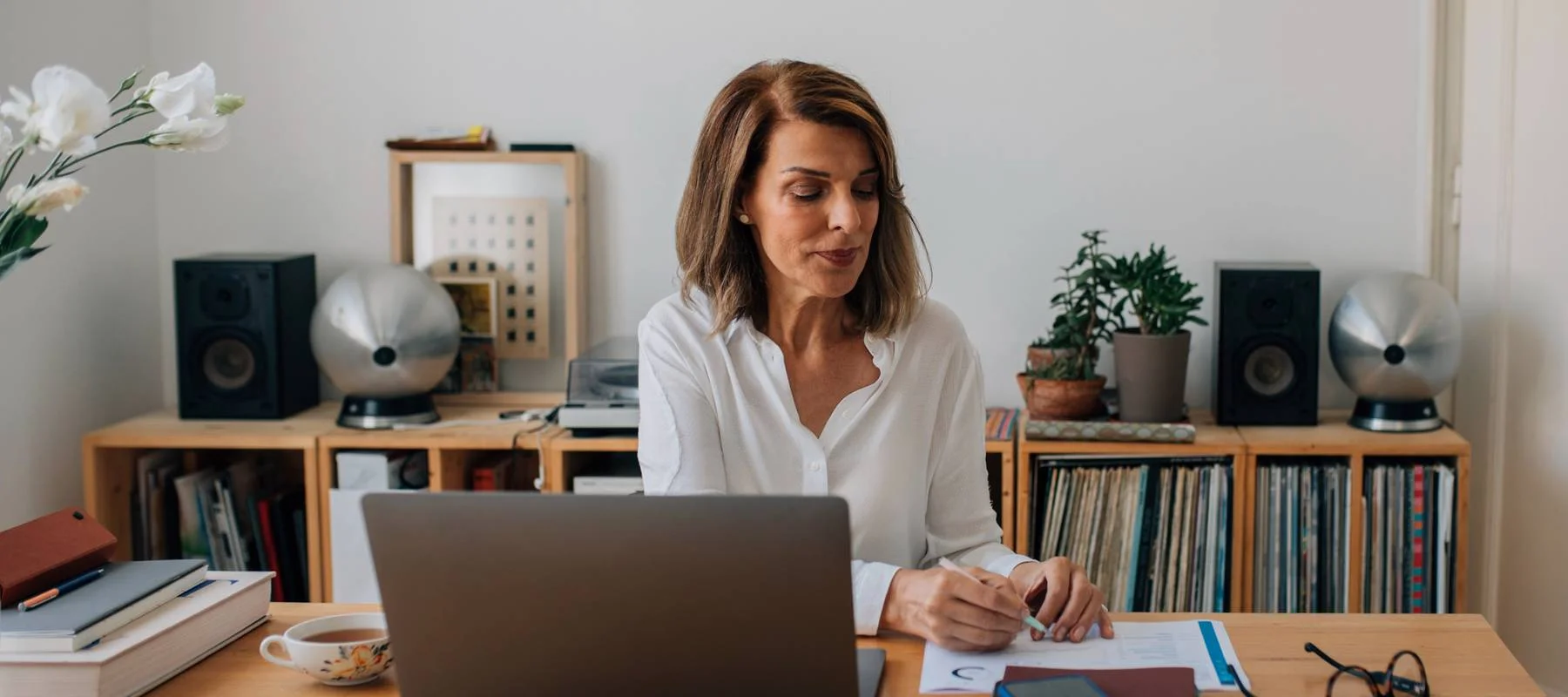 An executive assistant works thoughtfully from a home office, reviewing documents beside a laptop and coffee cup. The calm, organized workspace reflects the professionalism, dedication, and appreciation high-level executive assistants bring to the people and businesses they support.