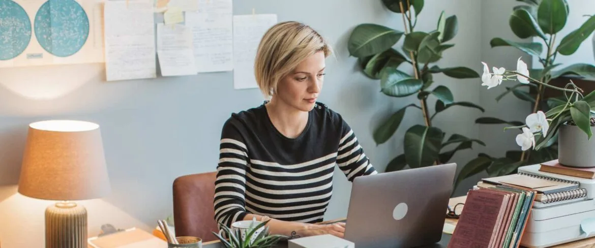 A professional executive assistant sits at a desk, focused on their work. The workspace is organized, with a laptop, notebook, and other office essentials neatly arranged, reflecting efficiency and attention to detail.