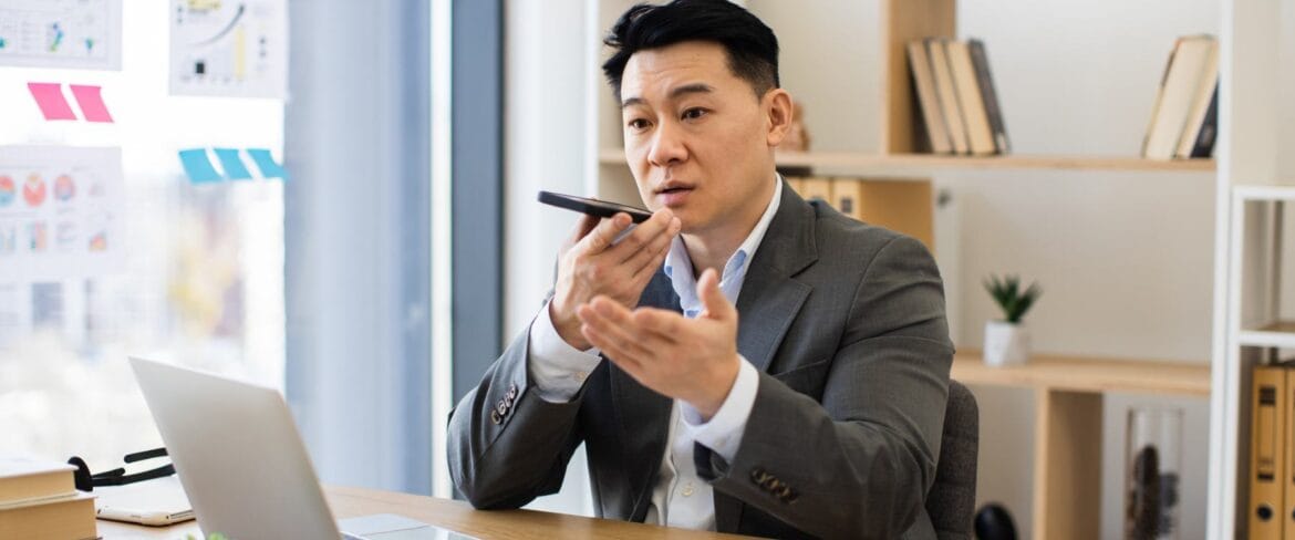 “Executive speaking into a phone while reviewing data in a modern office, illustrating how C-suite leaders rely on executive assistants to manage time and priorities.