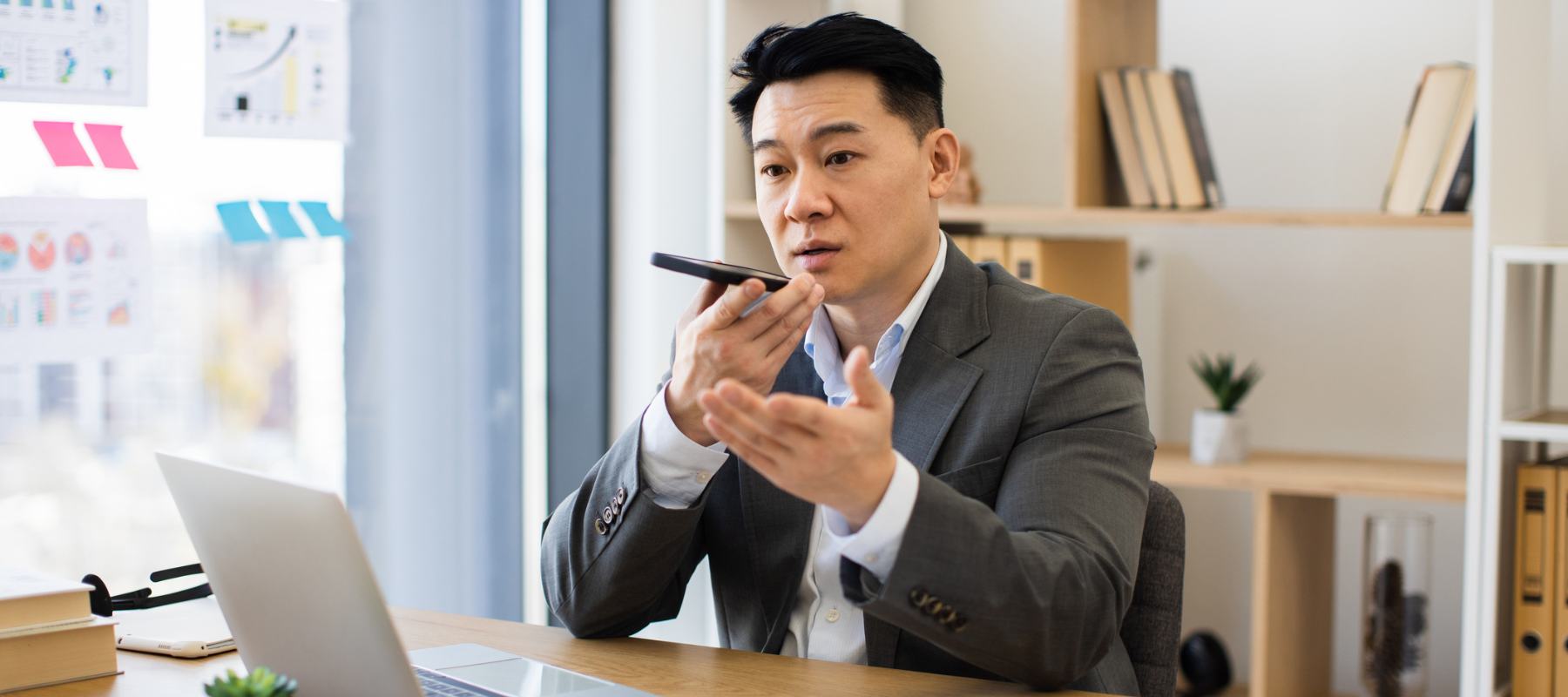 “Executive speaking into a phone while reviewing data in a modern office, illustrating how C-suite leaders rely on executive assistants to manage time and priorities.