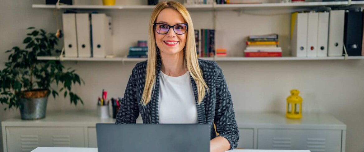 A professional executive assistant working on a laptop, managing schedules and calendars using AI tools in a modern office setting.