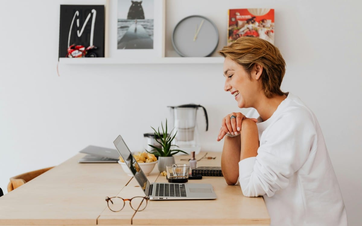 Smiling executive assistant working remotely from a bright home office, seated at a desk with a laptop, coffee, and workspace essentials. The image accompanies guidance on how to find a qualified executive assistant replacement during a leave of absence or role transition.